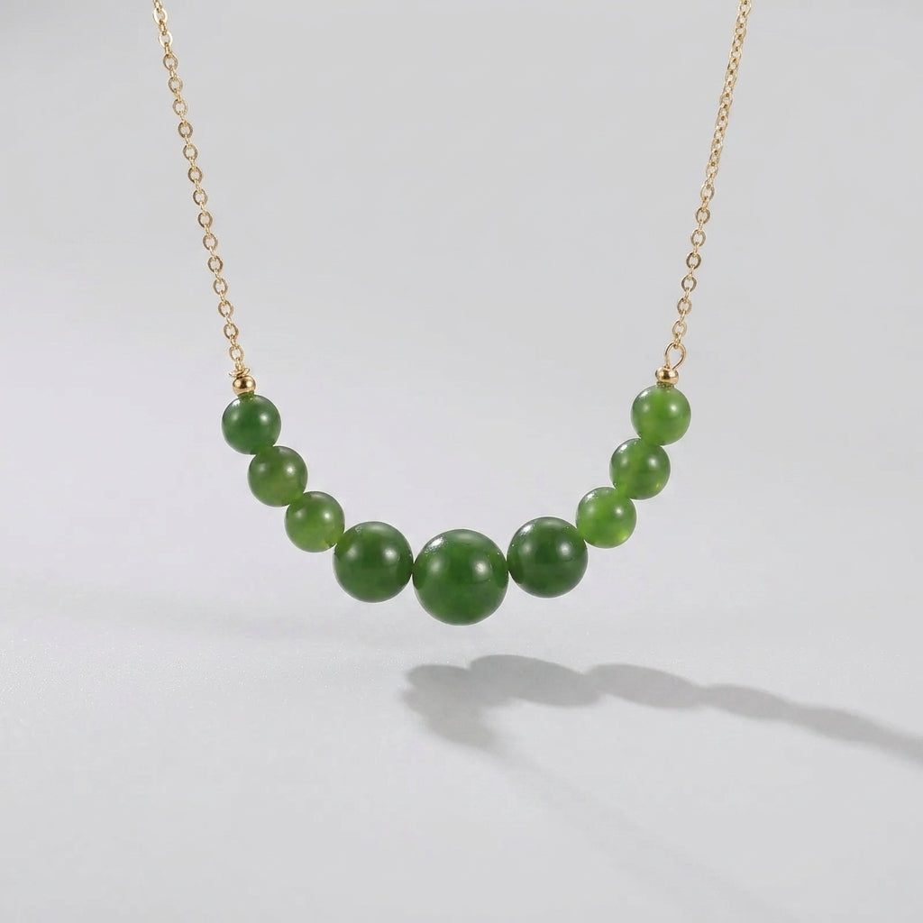 All Smiles necklace featuring a delicate gold chain with graduated green jade beads arranged in a gentle curve.
