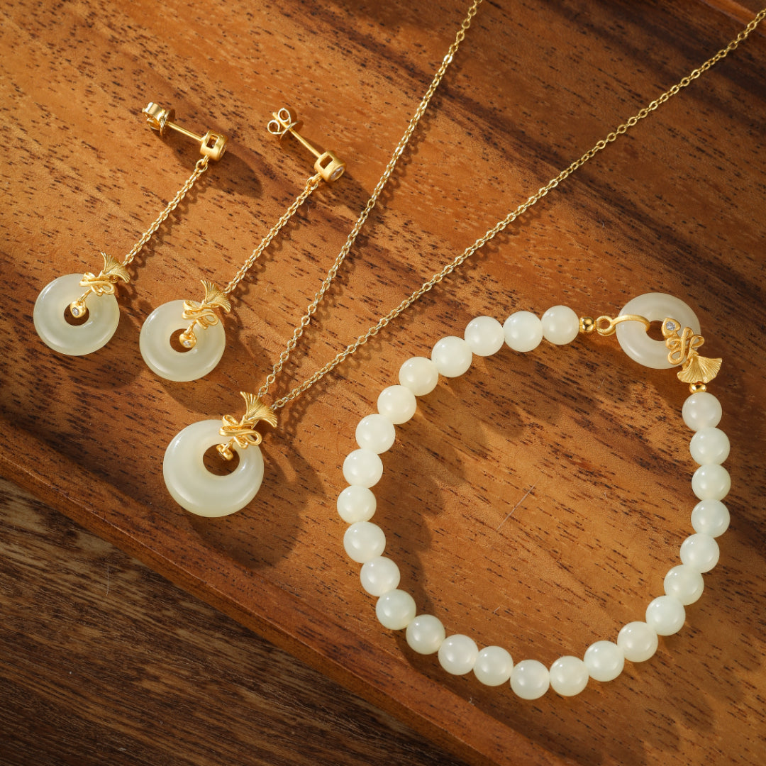 Charmed Life "Hetian Jade Bi Disc" beaded bracelet with pendant earrings and necklace on a wooden background