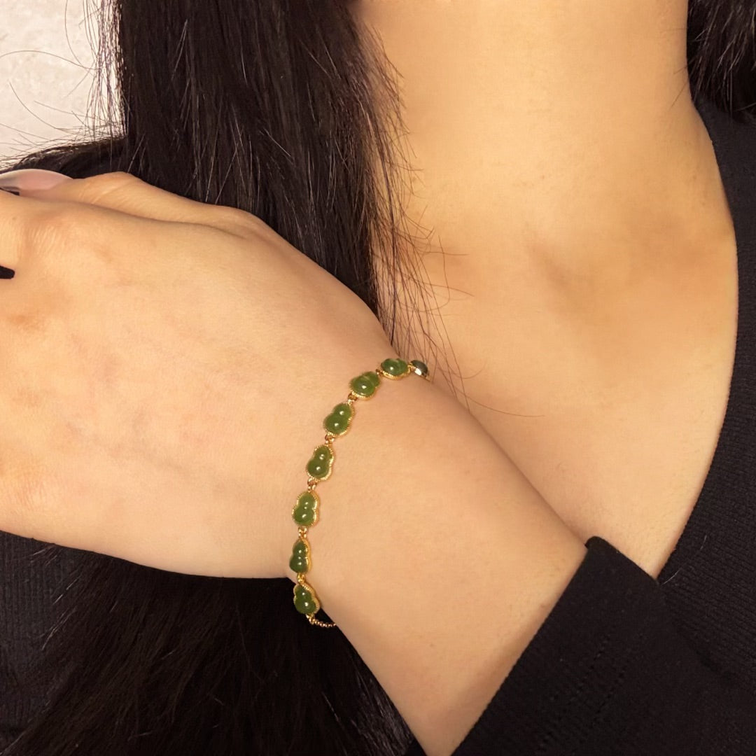 Green jade gourd-shaped charms on a gold-plated chain bracelet worn on a woman's wrist.