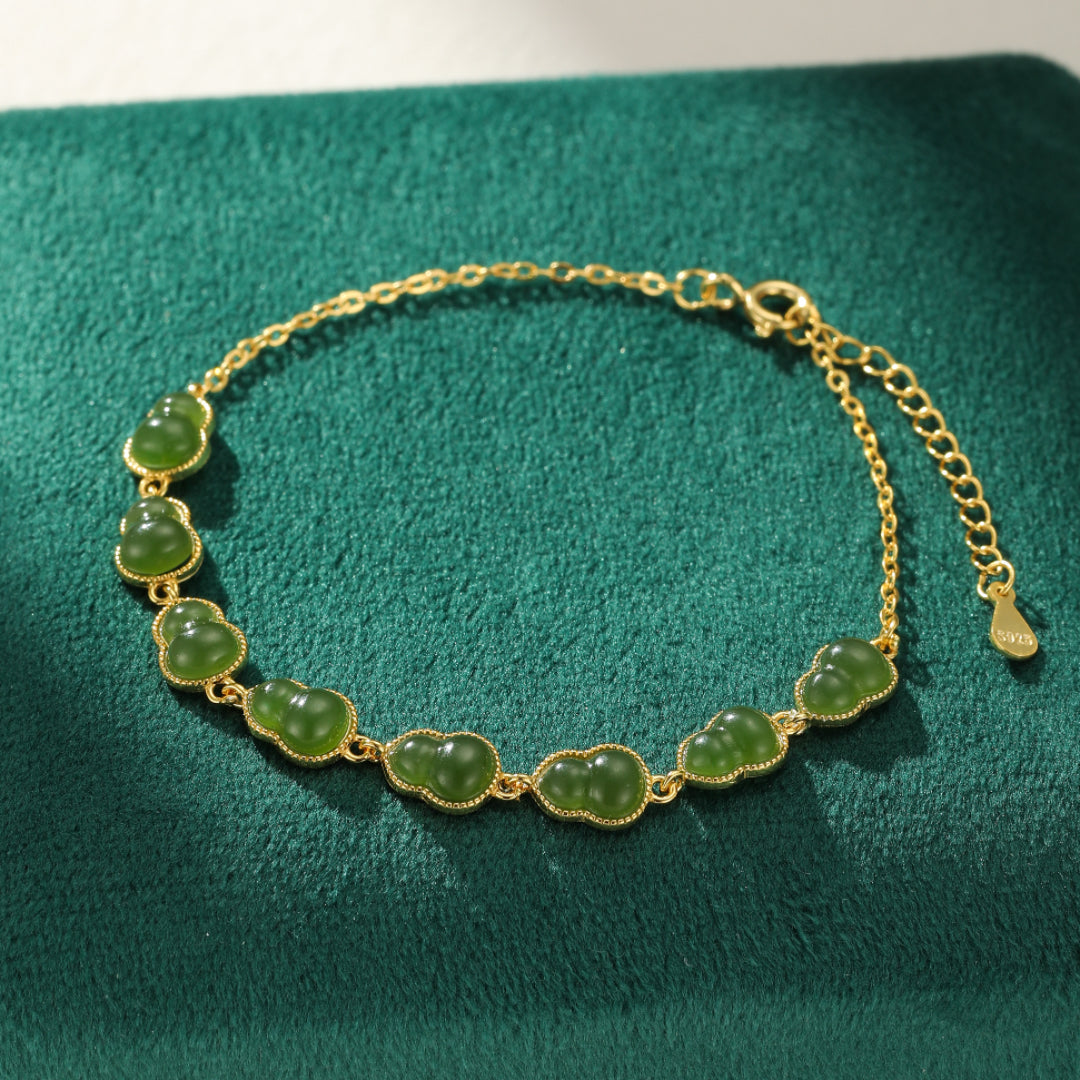 A delicate gold-plated silver chain bracelet featuring multiple small, polished green jade gourds linked together, laid on a green velvet surface.