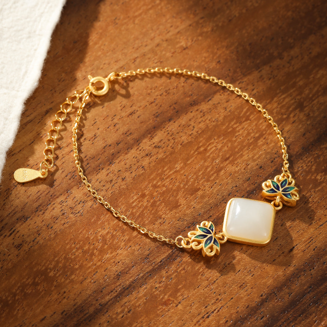 Gold plated silver bracelet featuring a square white Hetian jade stone with delicate blue lotus flower accents on a wooden background.