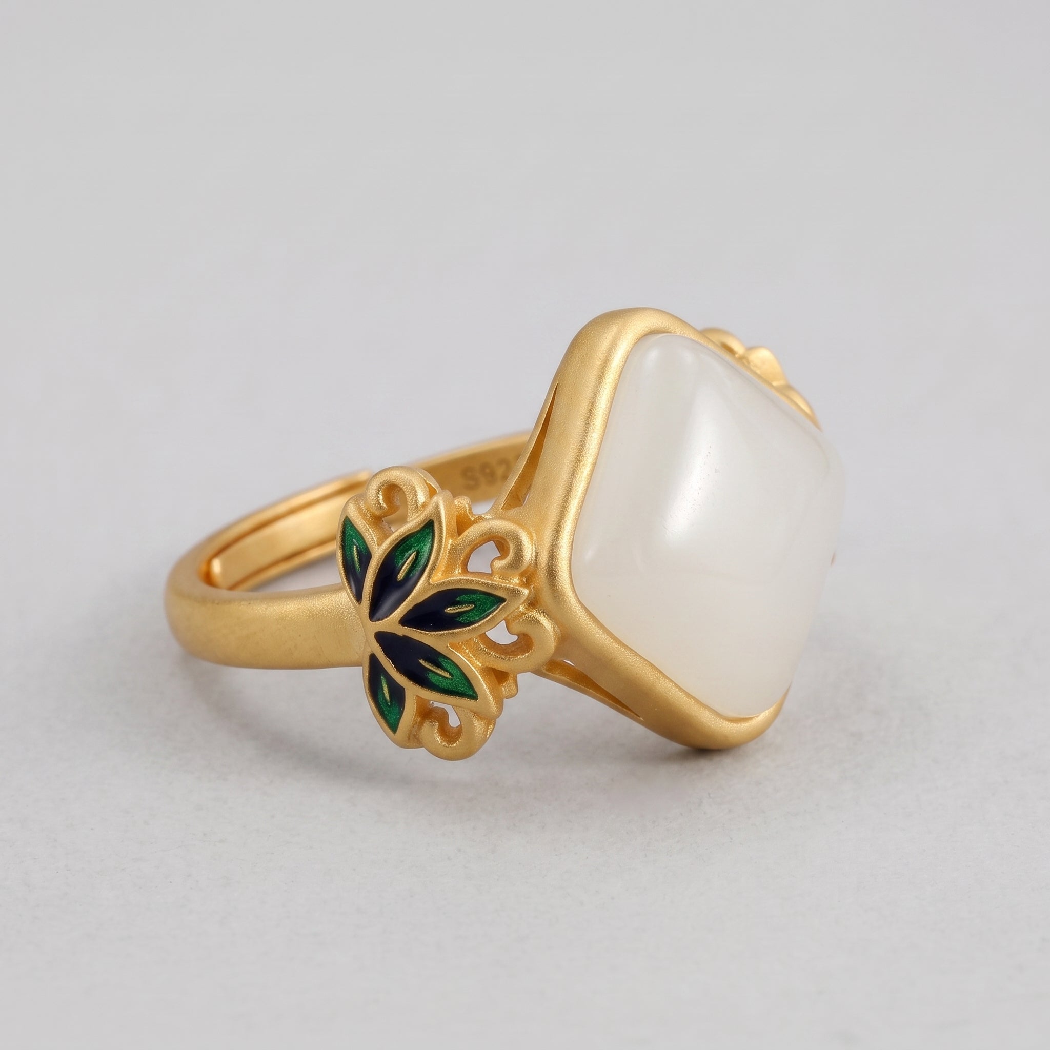Gold ring with a square white jade stone and floral details in green and blue enamel on the band.