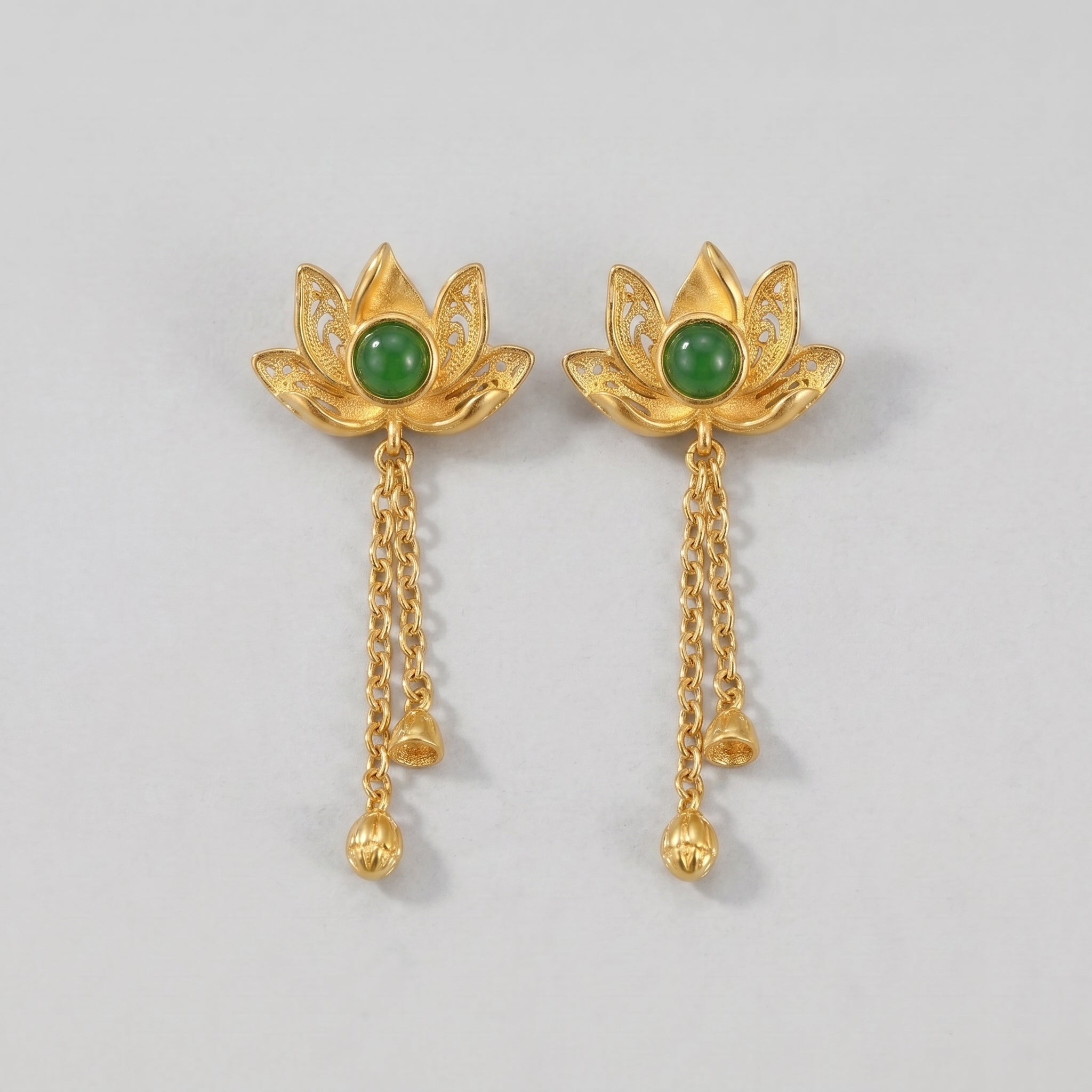 Evensong gold lotus drop earrings with green jade centers and dangling chains with small bells and lotus bud charms on a light gray background.