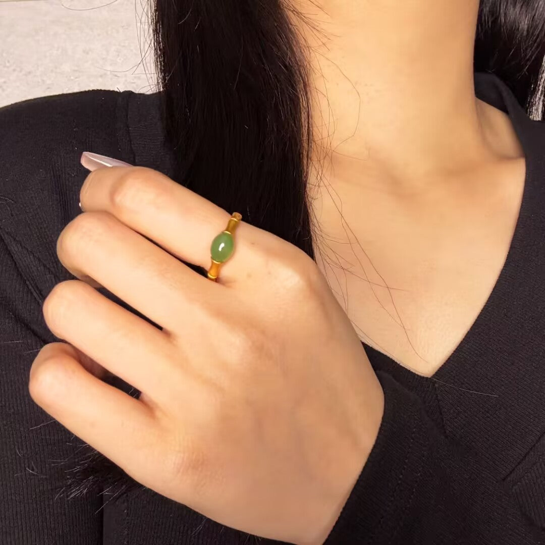 Gold plated silver ring with a green jade stone in a bamboo design, worn on a finger.