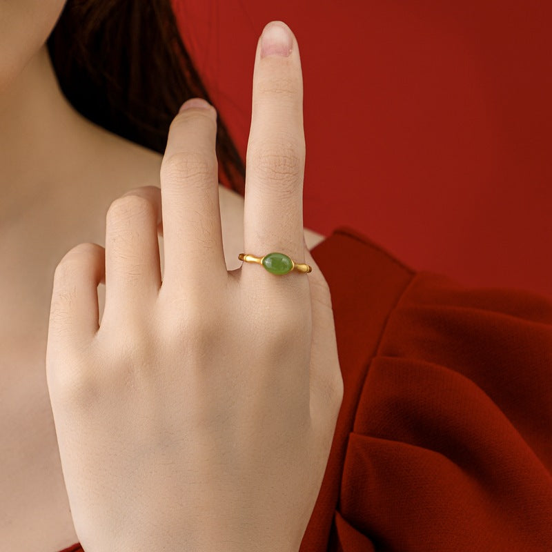 Gold ring with an oval green jade stone on a woman's ring finger.
