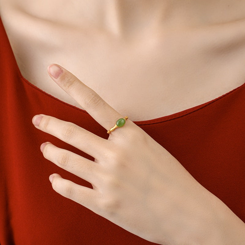 A gold ring with a green jade stone shaped like a bamboo shoot on a woman's finger.