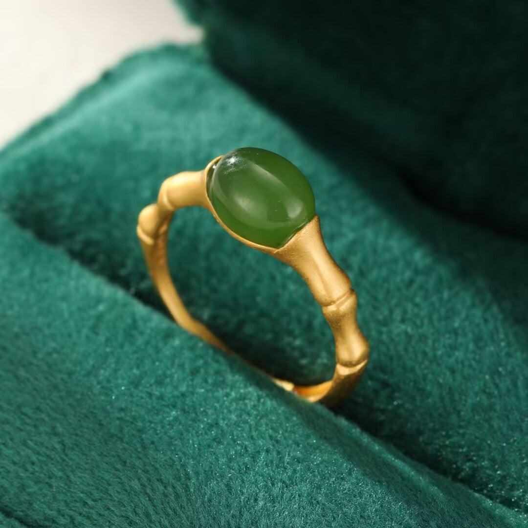 Close-up of a gold-plated silver ring designed to resemble bamboo, featuring a smooth, oval-shaped green jade gemstone set in the center.