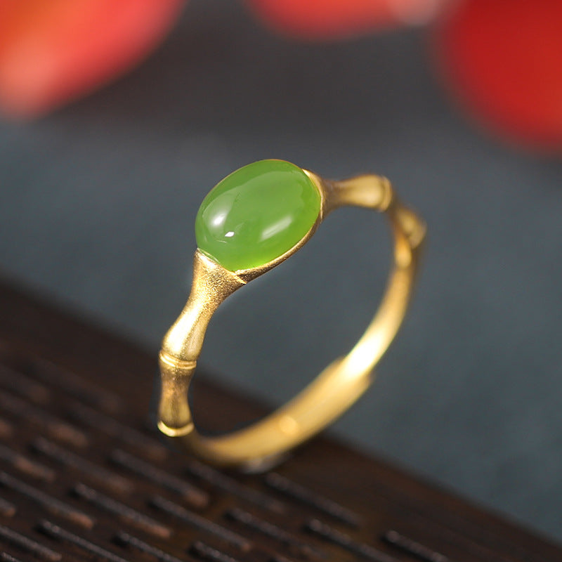 Gold ring with a bamboo design and a smooth, oval green jade stone set in the center.