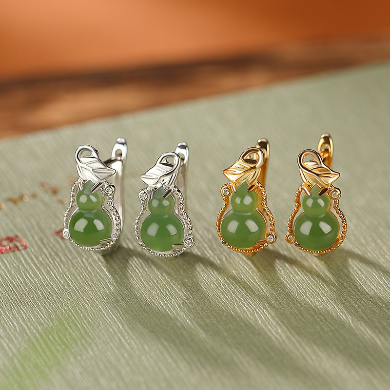 A pair of silver and a pair of gold gourd hoop earrings featuring green jade pendants and small clear crystals.
