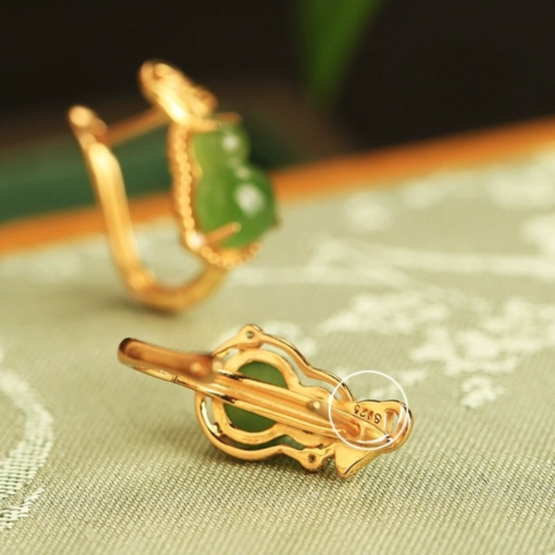 Close-up of gold-plated silver hoop earrings featuring green jade gourd charms and a "S925" stamp on the clasp.
