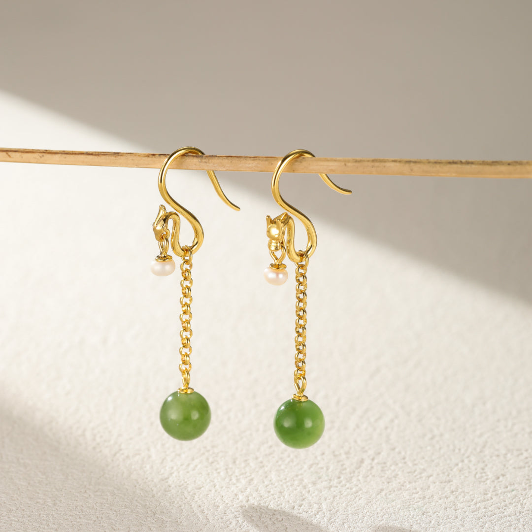Gold dragon-shaped earrings with a pearl and a green jade bead dangling from a delicate chains