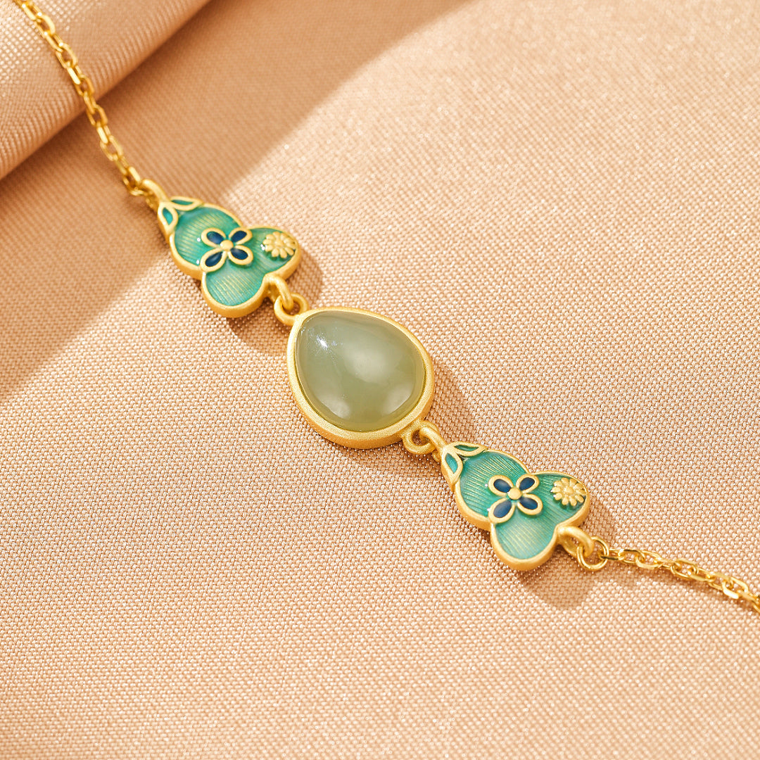 A delicate gold-plated silver bracelet featuring a central teardrop-shaped jade stone and two ornate gourd-shaped charms with blue and green enamel floral details.