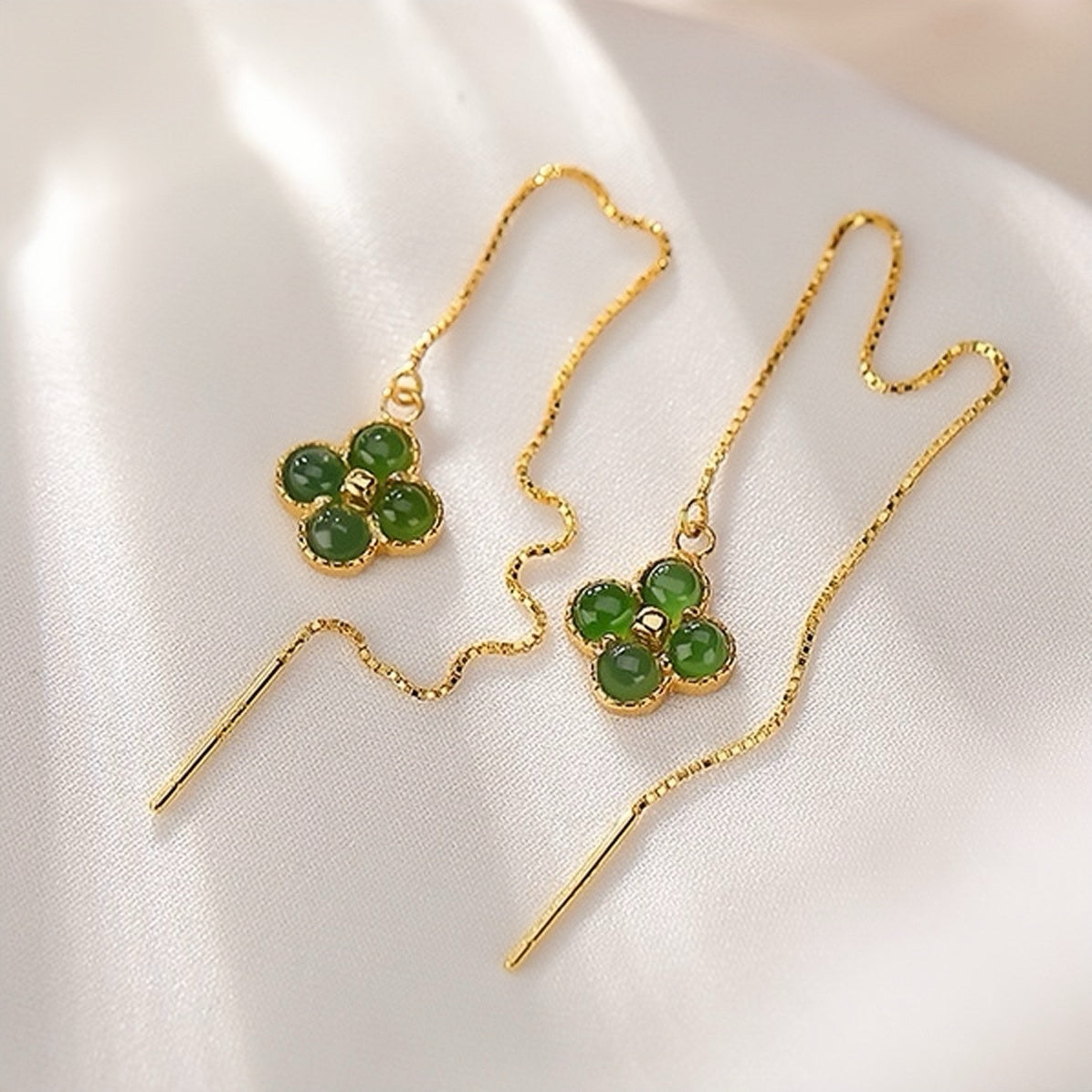 Lucky Streak green jade clover drop earrings with gold plated chains on a white satin background