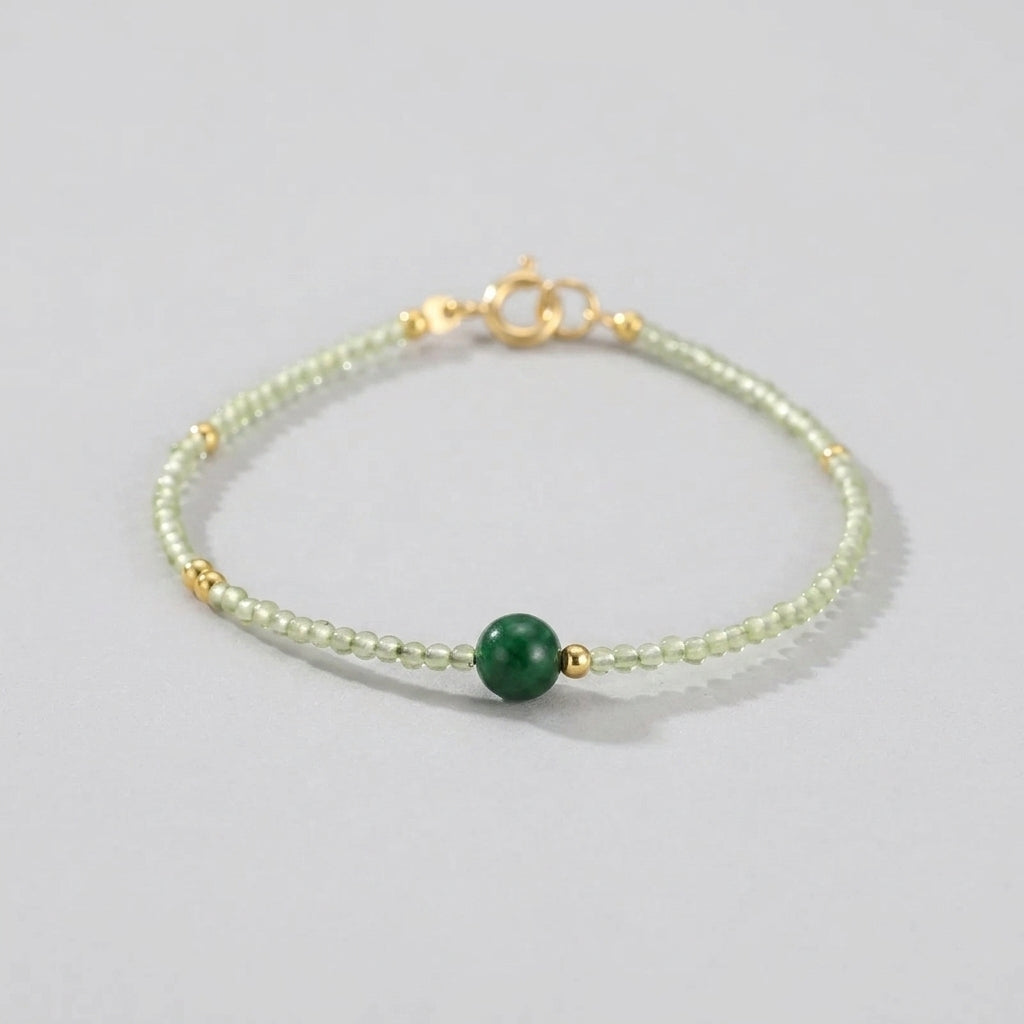 Delicate bracelet with small light green beads and gold accents, featuring a single, larger dark green jade bead in the center.
