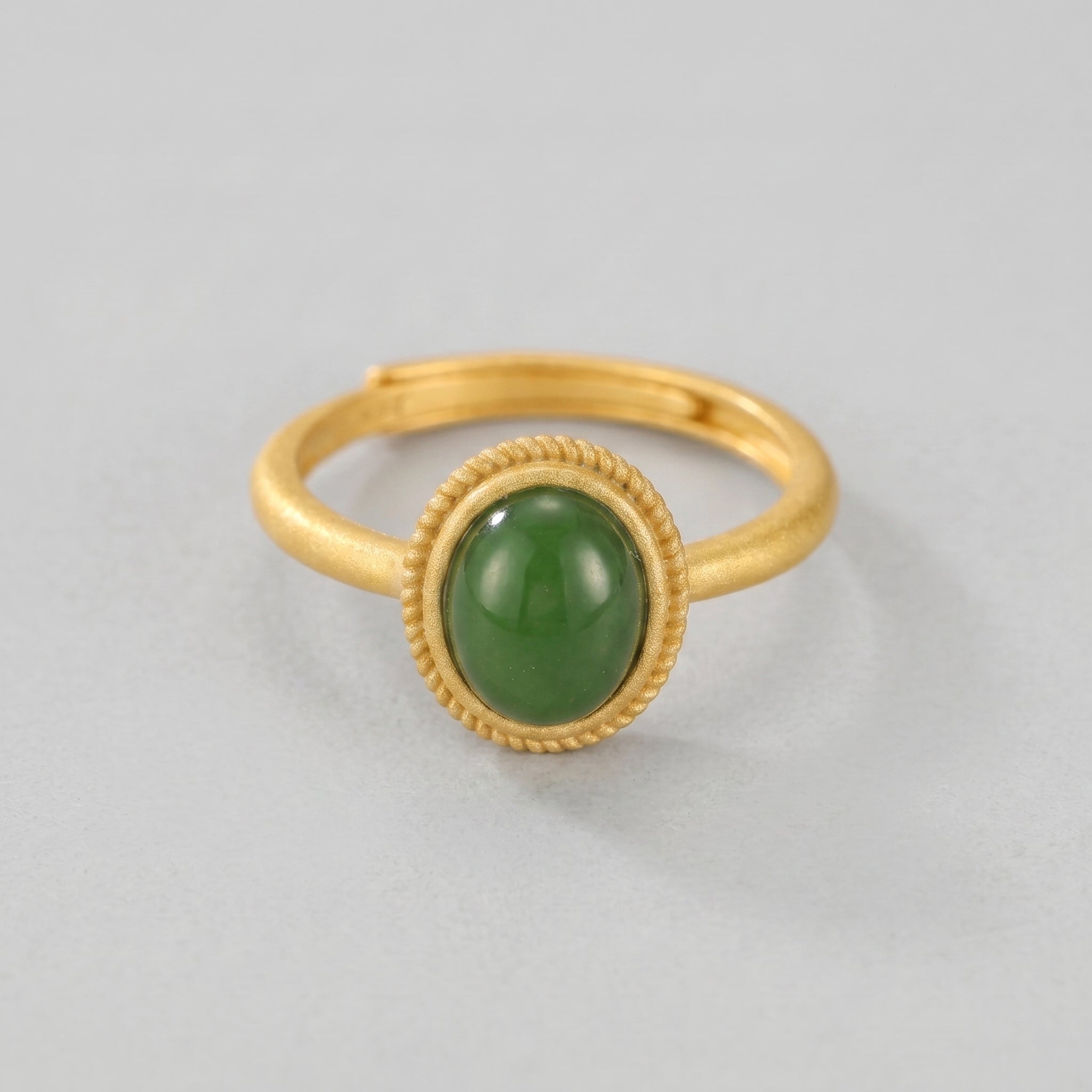 New Day gold ring with a smooth, oval green jade cabochon gemstone set in a textured bezel on a plain band.