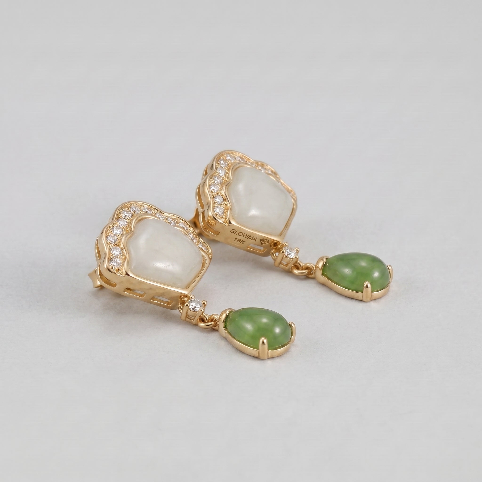 Close-up of elegant gold earrings featuring white jade and green jade teardrop pendants, accented with small diamonds.