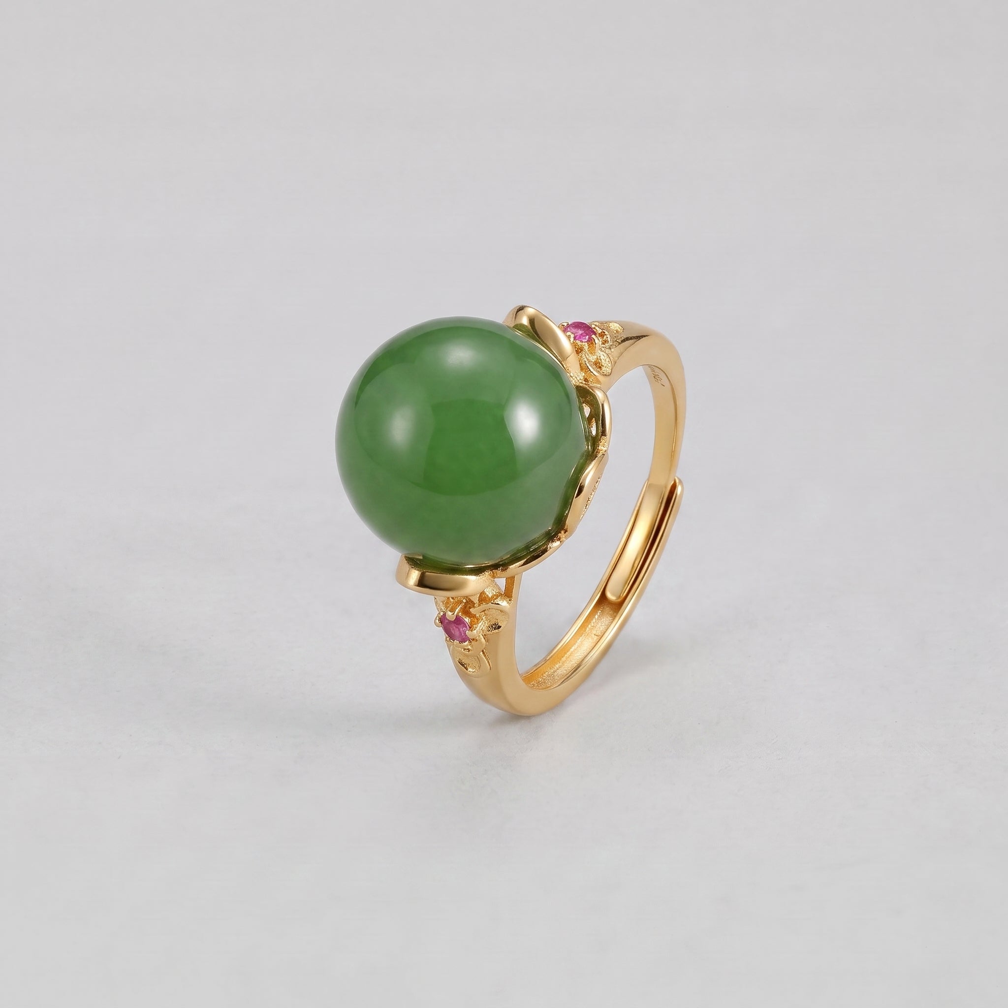 Sovereign ring with a large, round, vibrant green jade stone set in a gold band. The band is accented with small, pink gemstones on either side of the jade.