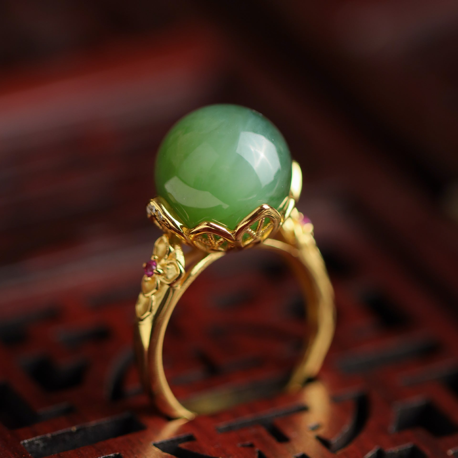 Sovereign ring with a smooth, round green jade stone set in a gold band with intricate floral details and small ruby accents.