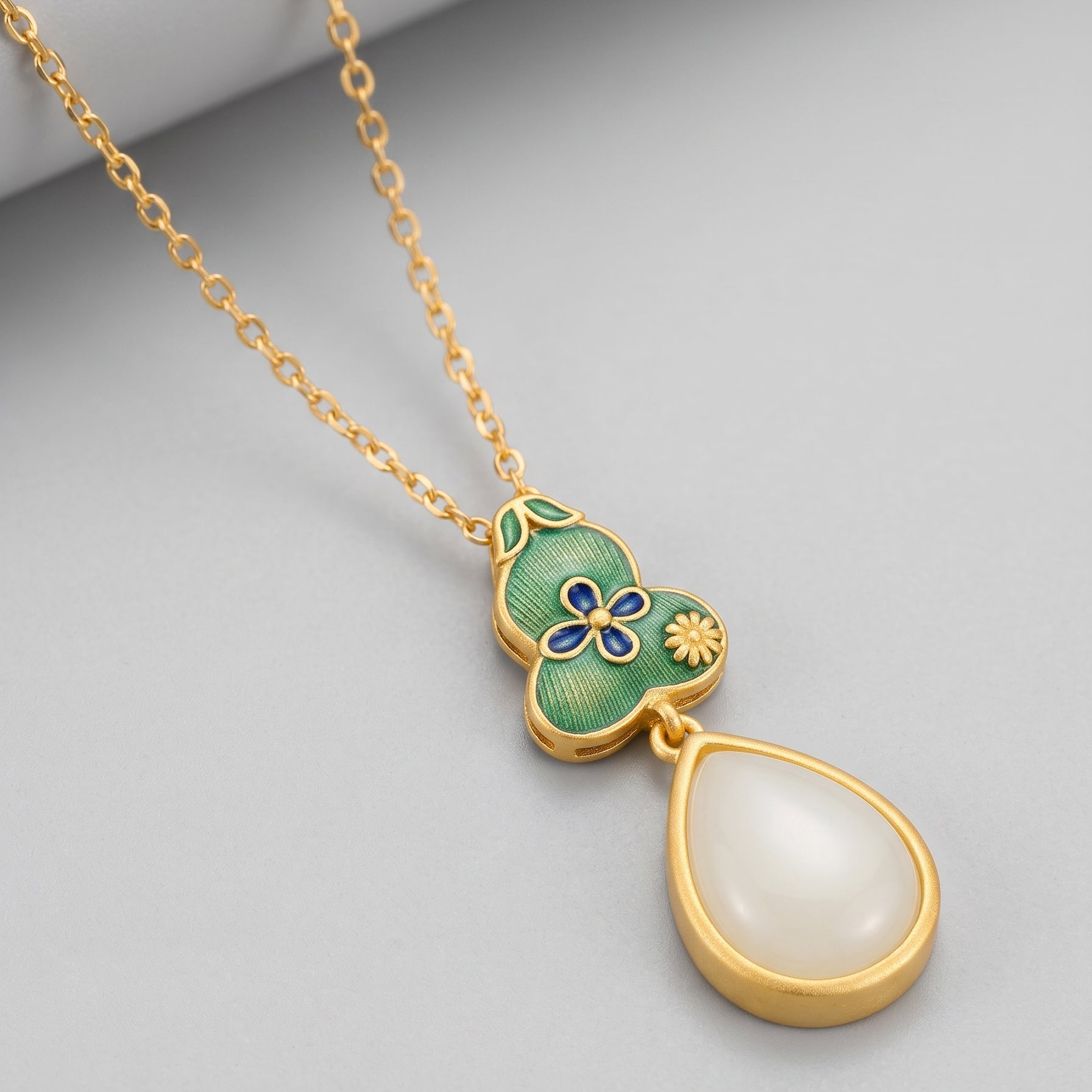Gold necklace with a green gourd pendant adorned with blue and yellow flowers, featuring a teardrop-shaped white jade stone.