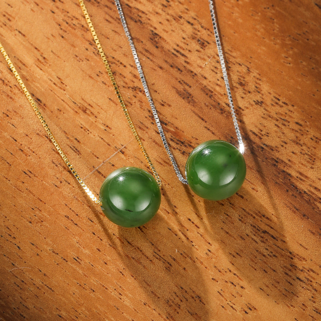 Two Acorn Green Jade Pendant Necklaces on delicate sterling silver chains, displayed on a warm wooden surface.