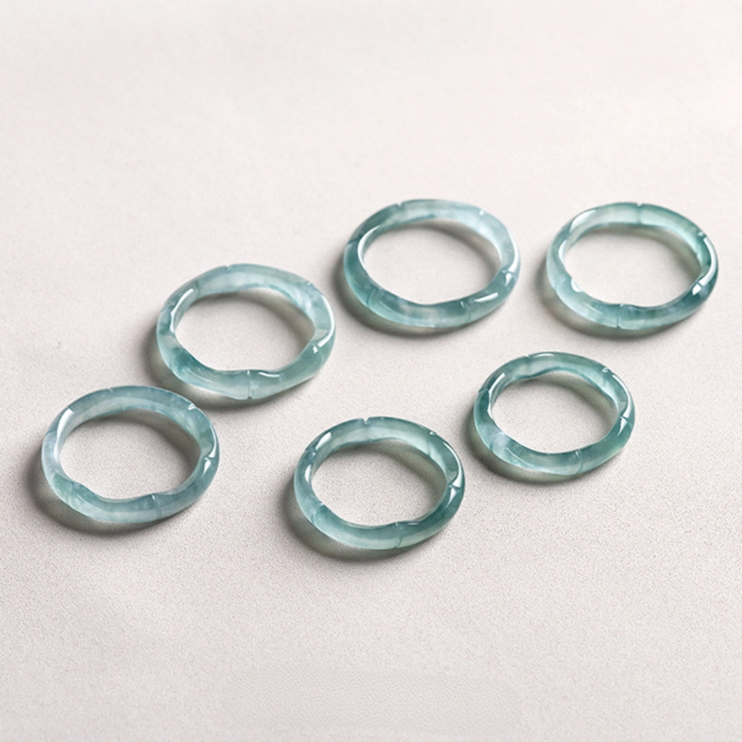 Six light blue jade bamboo rings with swirling white patterns, arranged on a light gray surface.