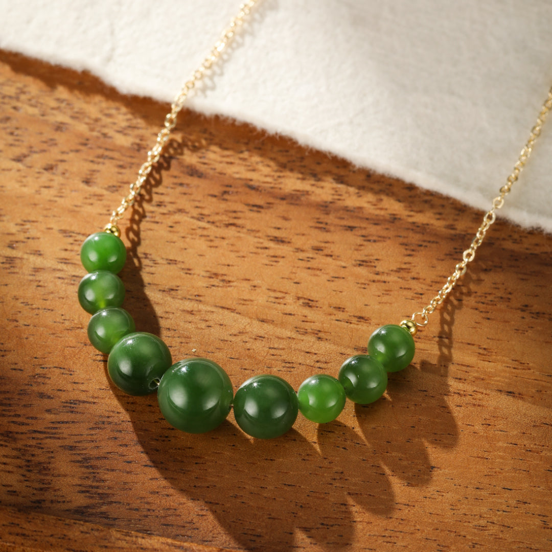 All Smiles Green Jade Beaded Necklace on a gold chain, featuring graduated beads with varying shades of green, laid on a wooden surface.
