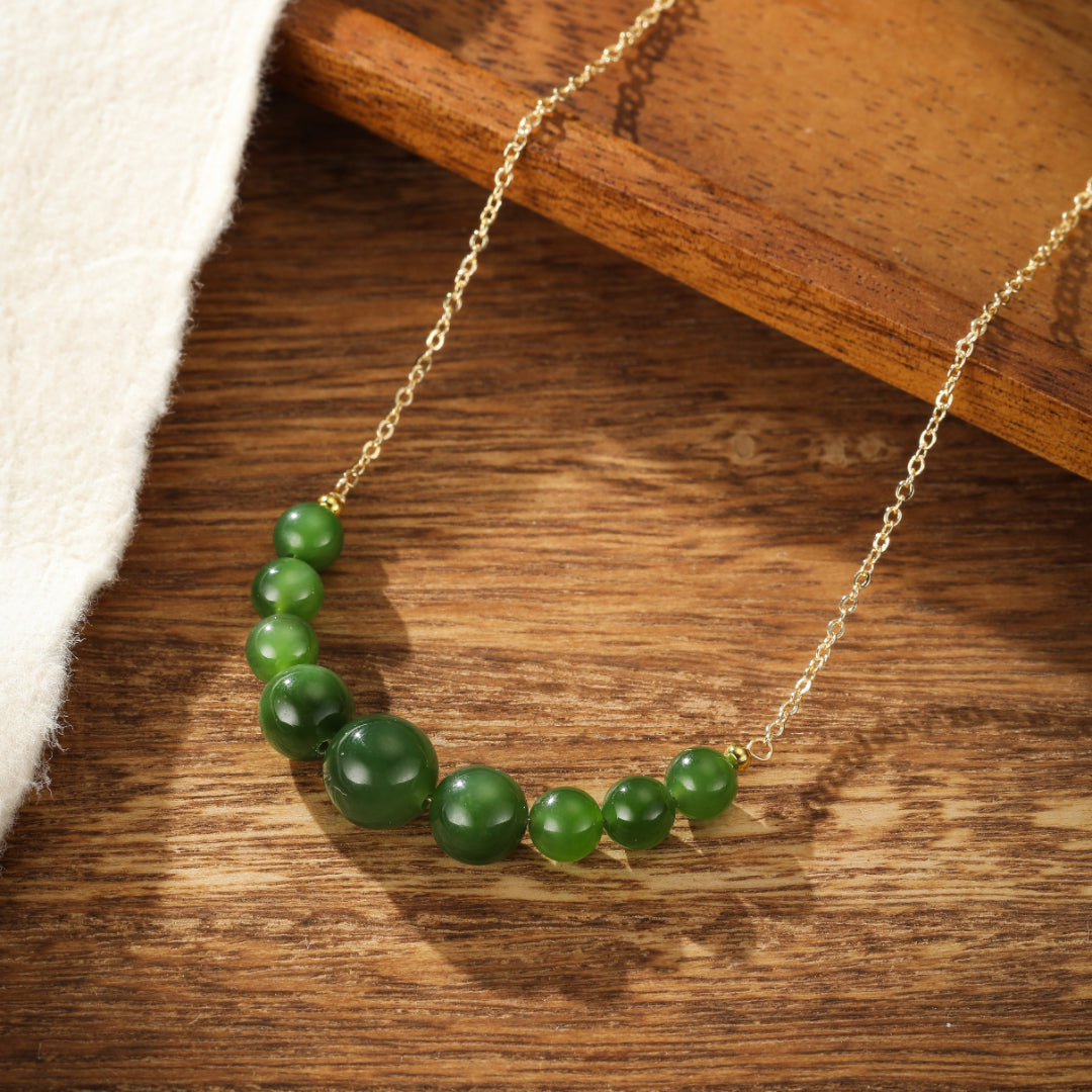 All Smiles green jade beaded necklace with a gold chain, laid out on a wooden surface.
