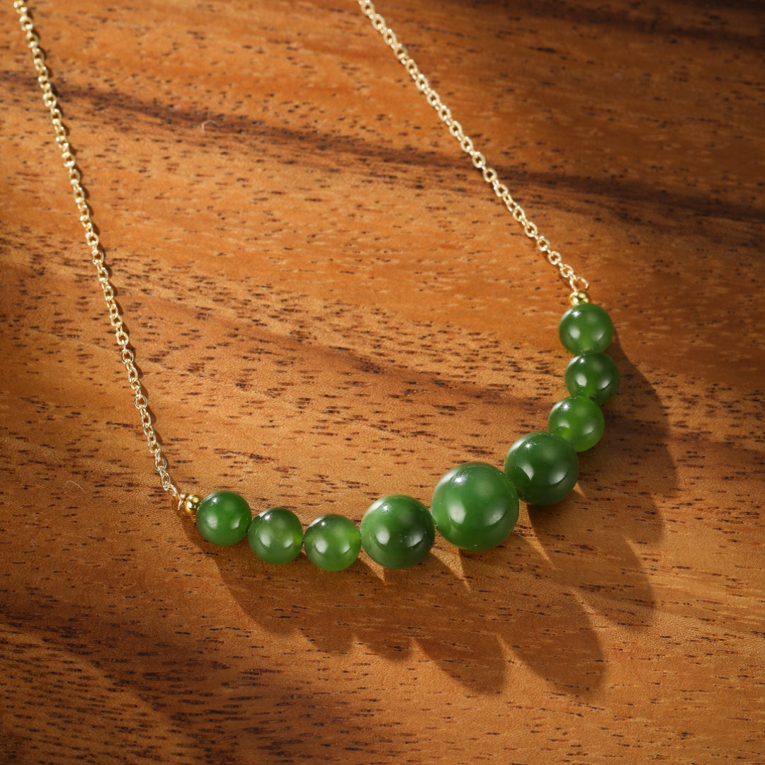 All Smiles green jade beaded necklace with a delicate gold chain on a wooden background.