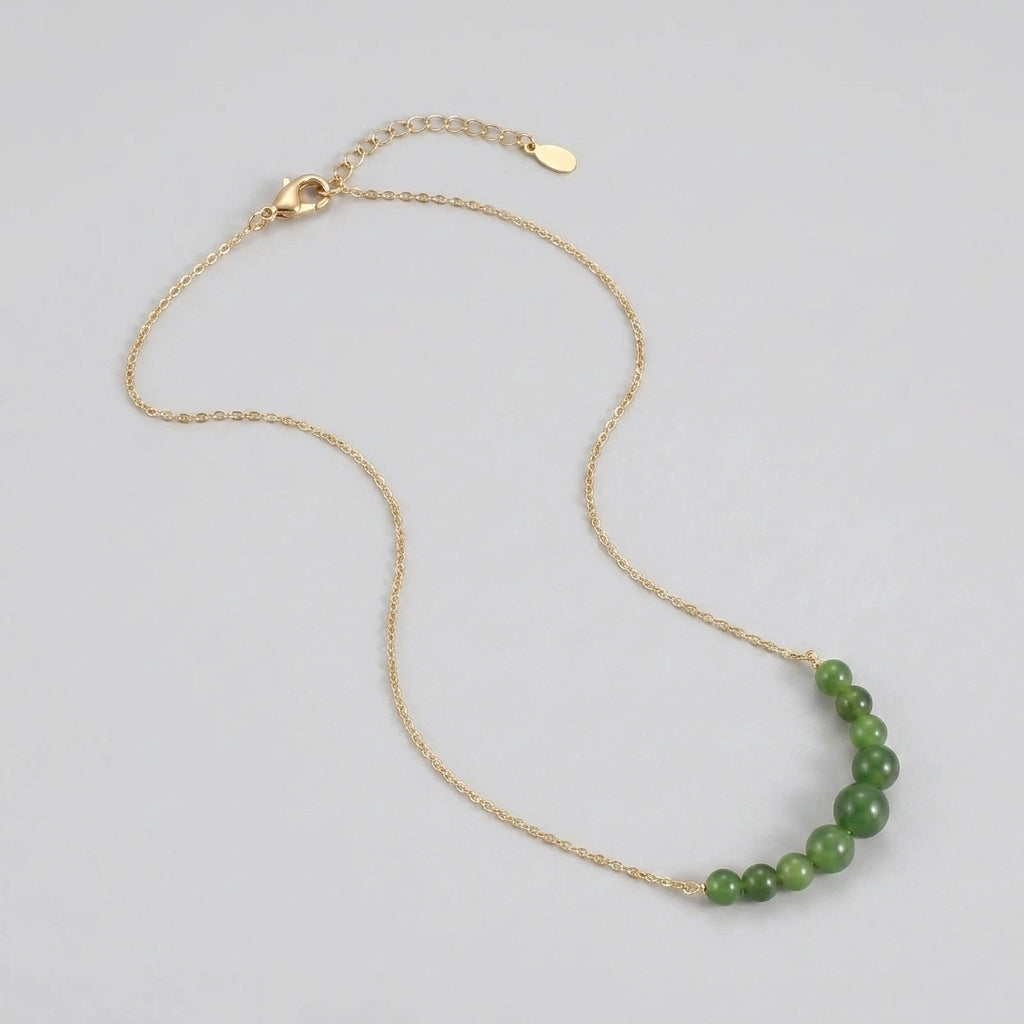A delicate gold chain necklace featuring a gradient of small, smooth green jade beads.