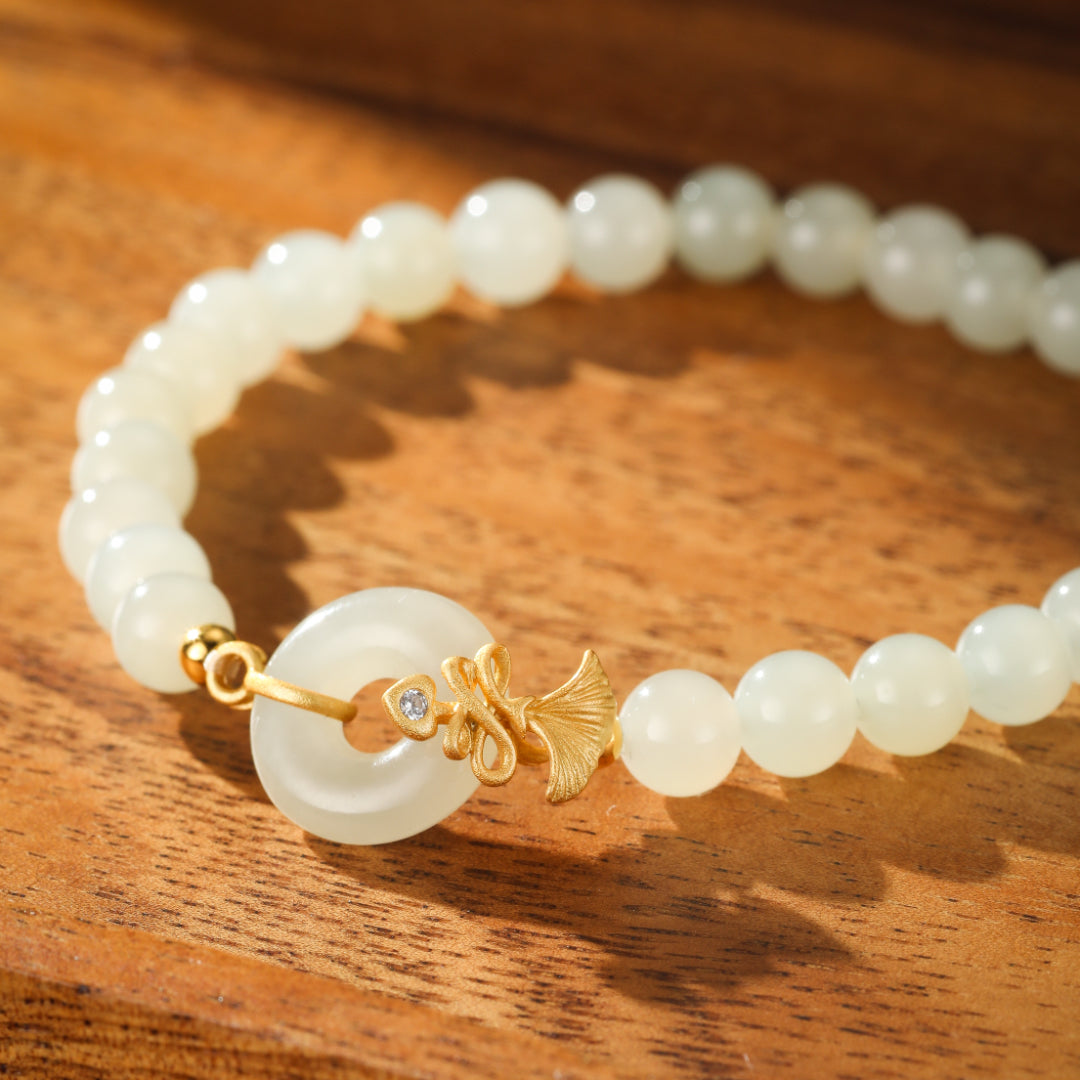 Charmed Life bracelet featuring a white Hetian jade bi disc charm with a gold-plated fish charm and a small diamond accent, strung on white jade beads.