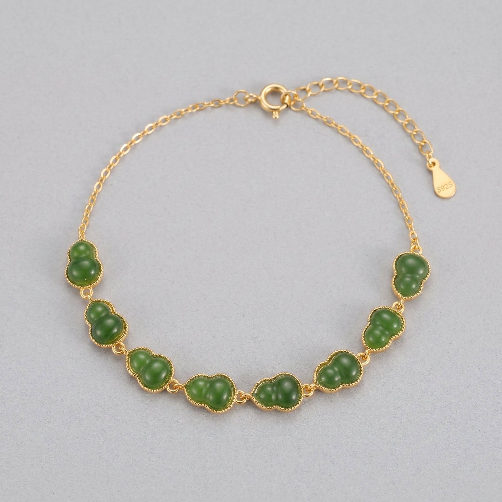 Gold bracelet with multiple green jade gourd charms on a grey background