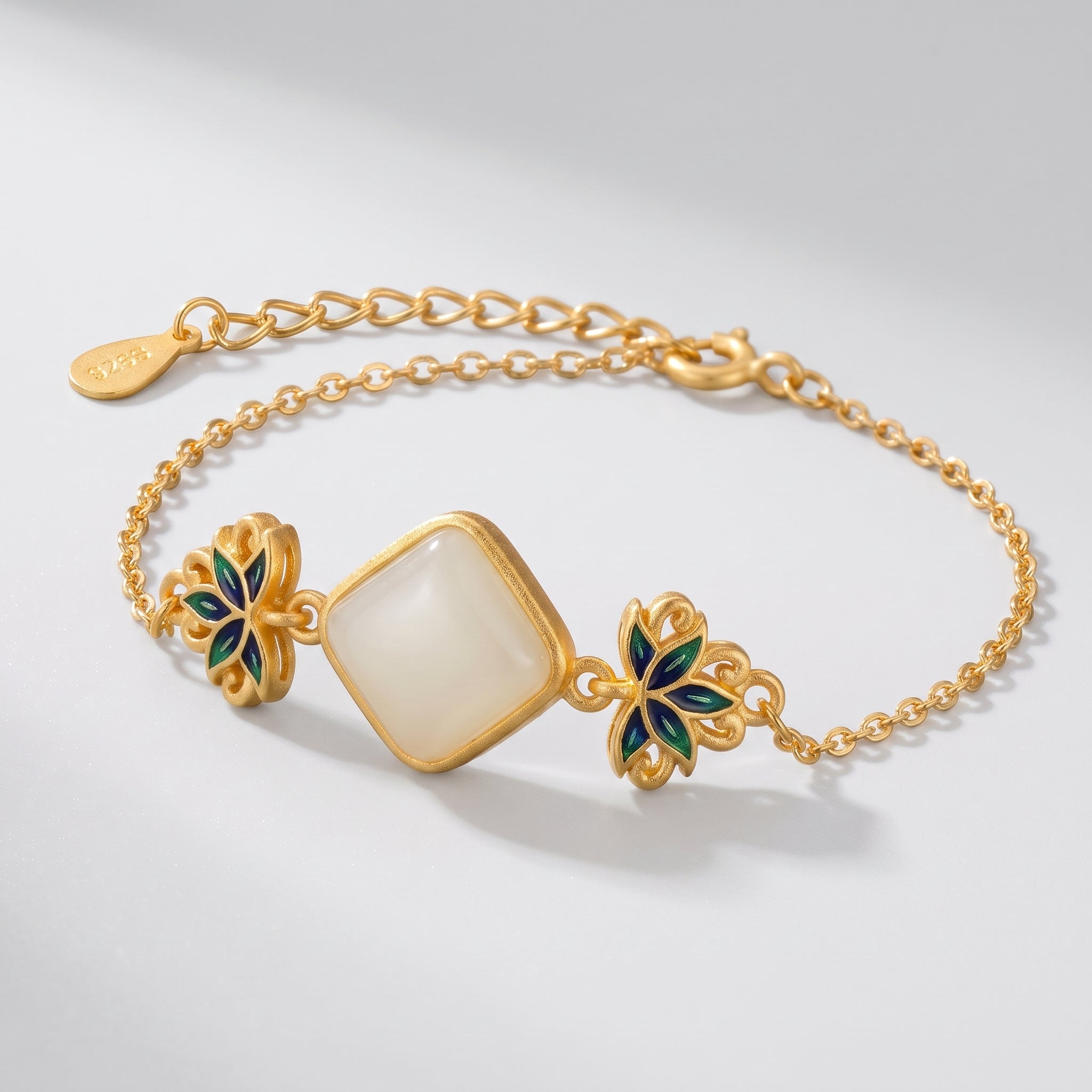 Gold bracelet featuring a square white jade stone centerpiece with intricate blue and green lotus flower accents on a delicate chain.