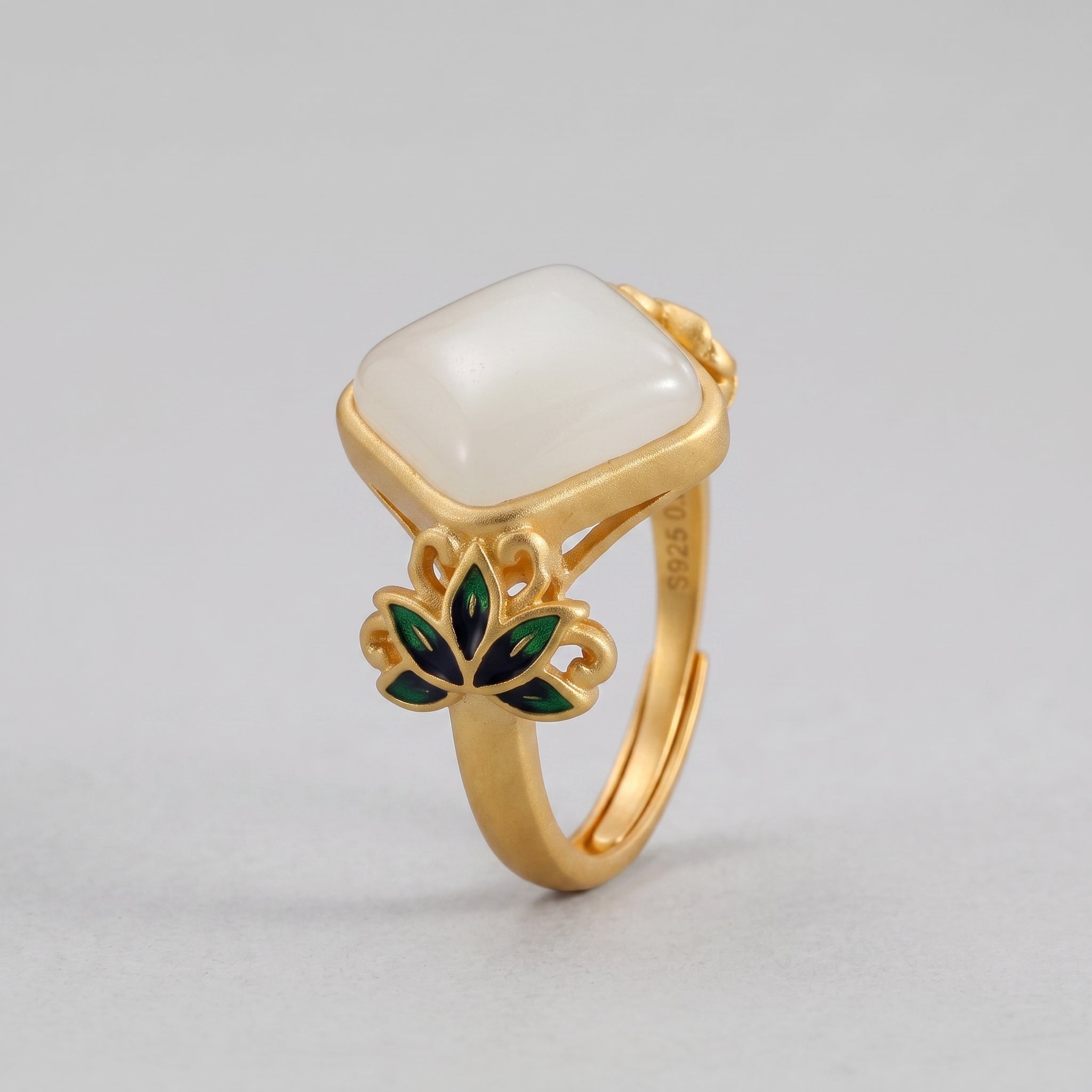A gold ring with a square, white Hetian jade stone, adorned with green and blue lotus flower details.