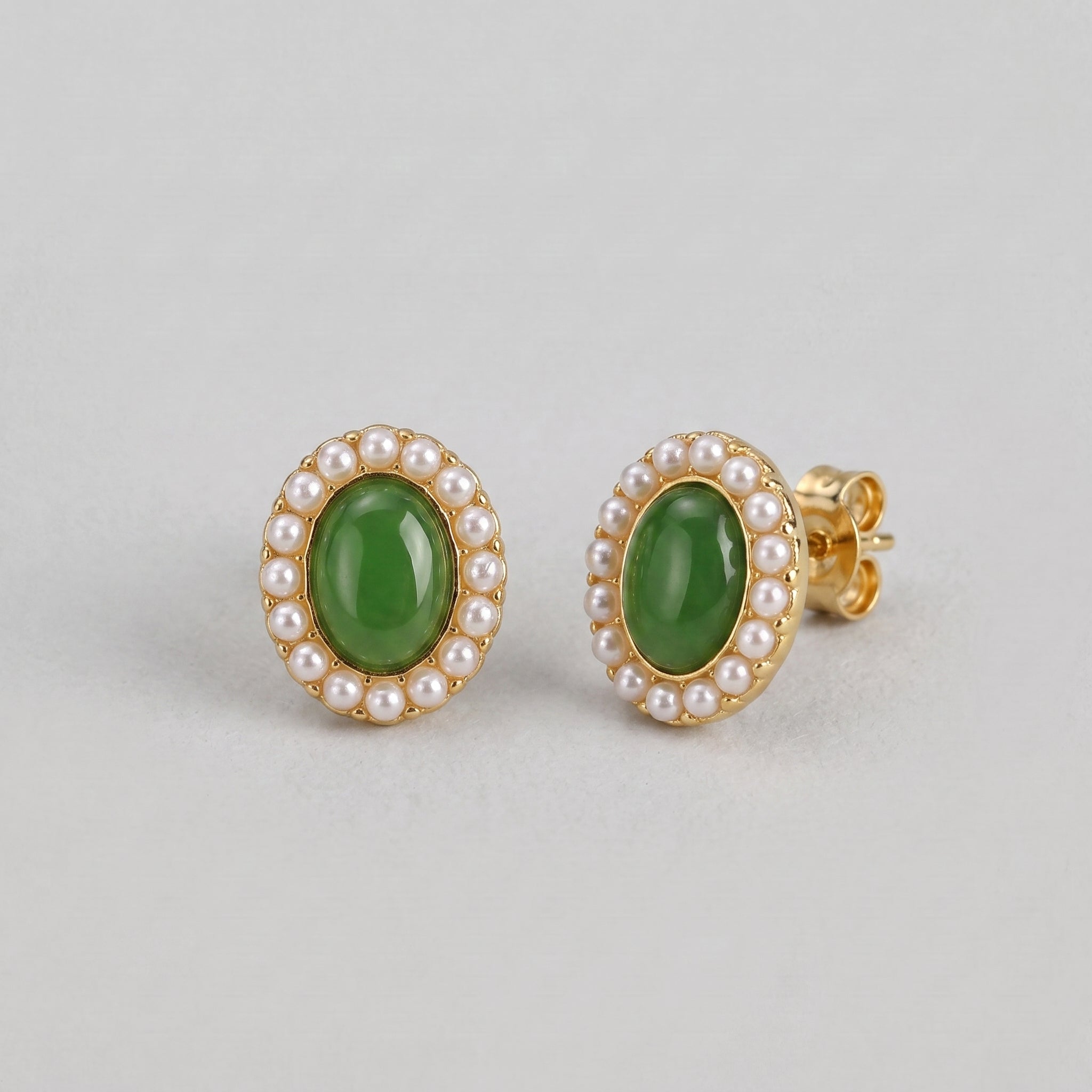 A pair of oval green jade sun stud earrings surrounded by small pearls on a light gray background.