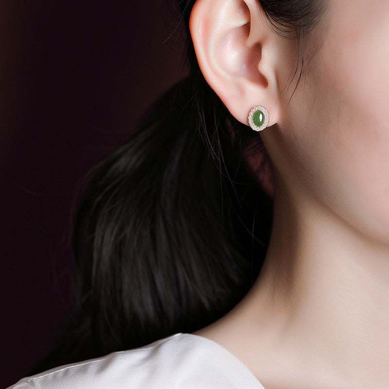 Close-up of a woman wearing oval green jade sun stud earrings with a halo of small diamonds.