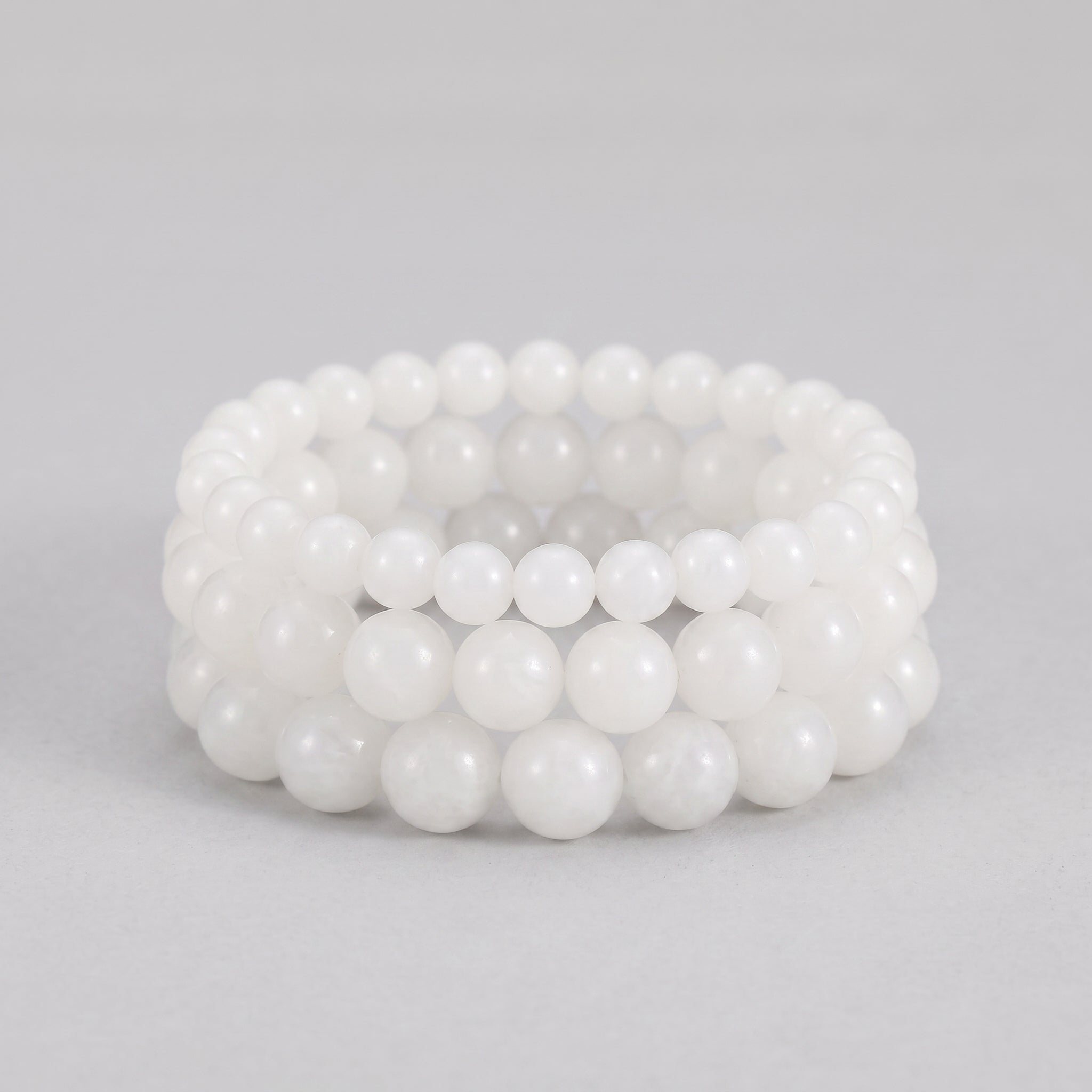 Three stacked white beaded bracelets made of Hetian jade on a grey background.