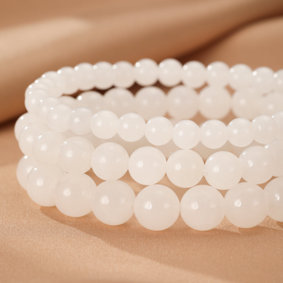 Three stacked bracelets made of smooth, white Hetian jade beads on a beige satin background.