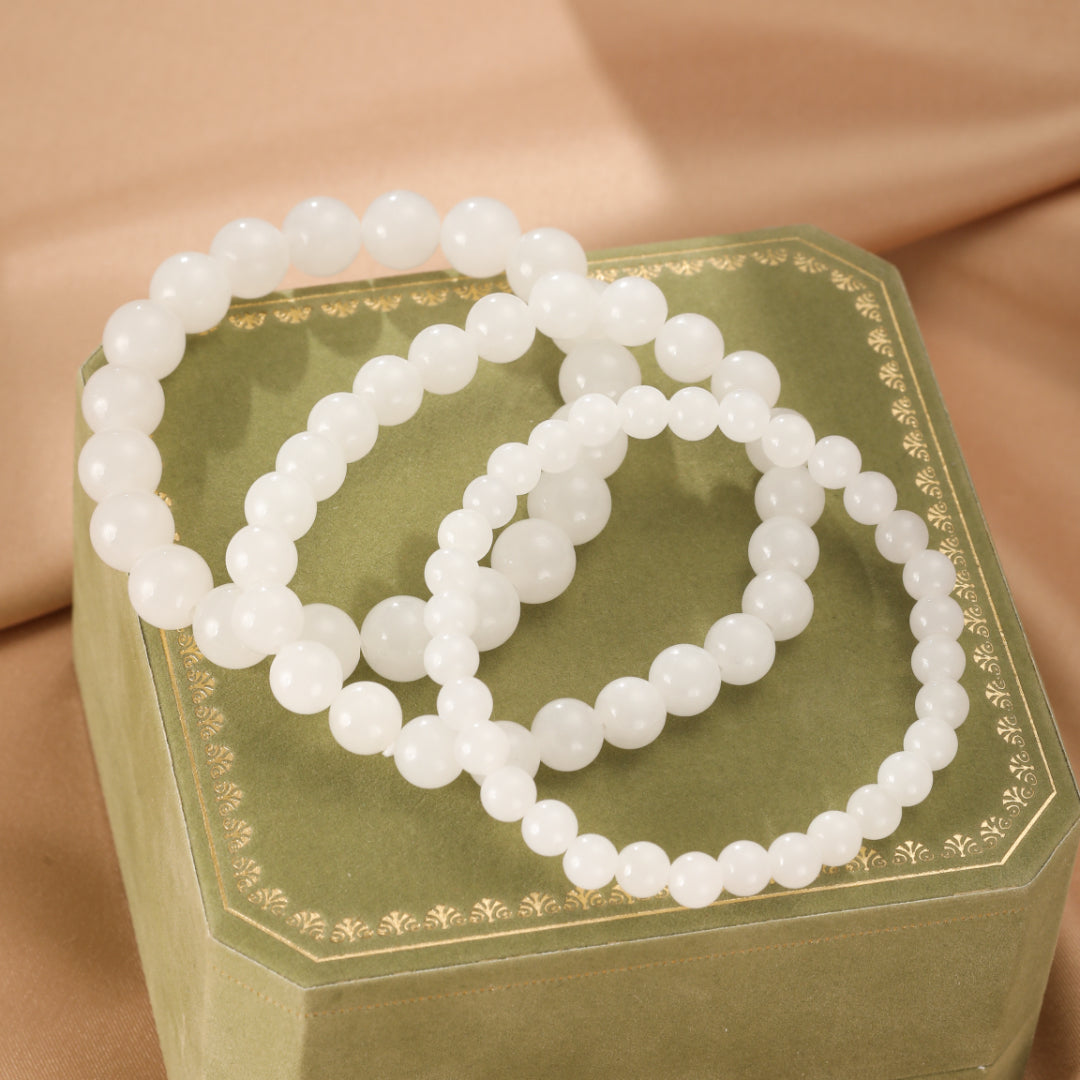 Three strands of white Hetian jade beaded bracelets are displayed on a green velvet jewelry box with gold trim.