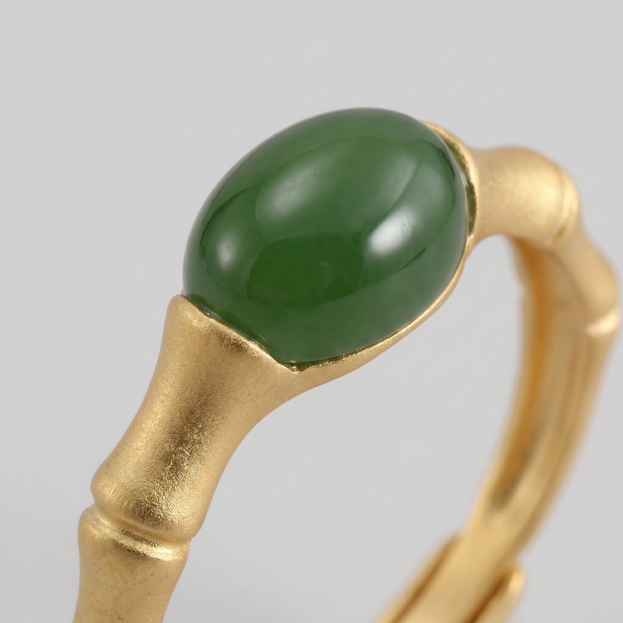 Close-up of a gold bamboo-style ring featuring a polished oval green jade gemstone.