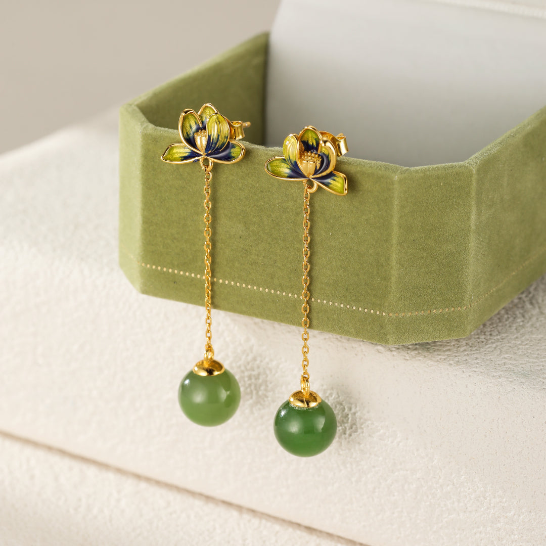 Halcyon green jade lotus drop earrings featuring delicate gold chains with smooth, round jade beads and intricately designed lotus flower tops with blue and yellow enamel accents.