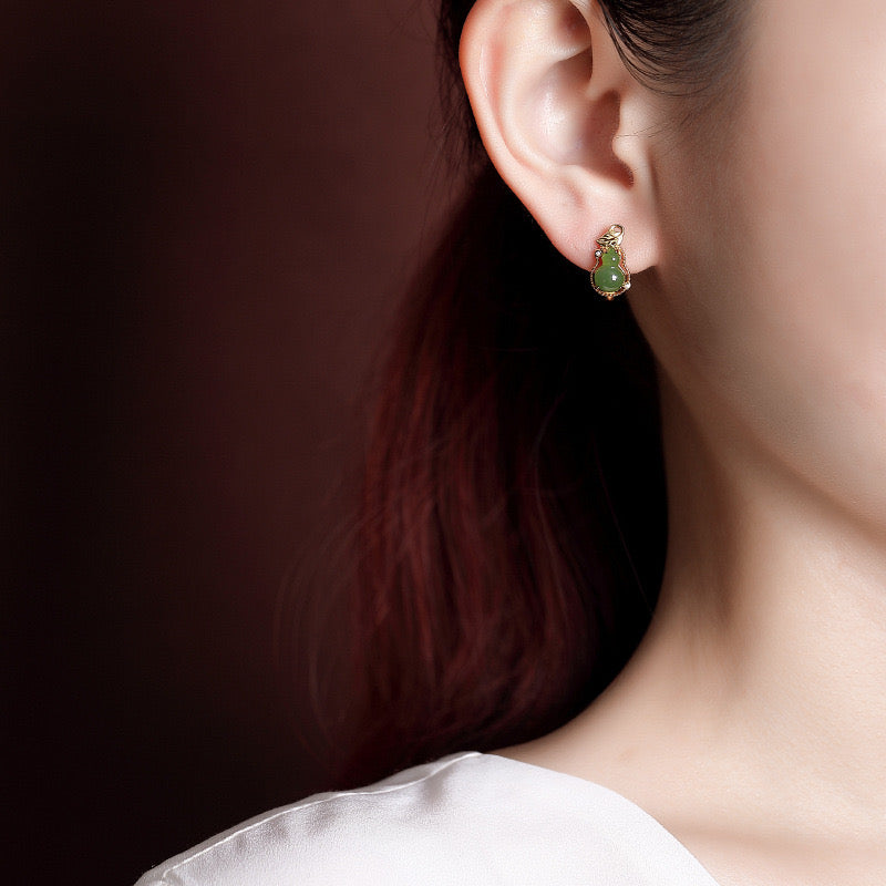 Close up of a woman's ear wearing gold-plated silver hoop earrings with green jade gourd charms.