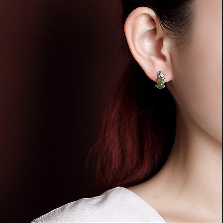 Close-up of a woman's ear wearing a pair of green jade gourd hoop earrings, showcasing their intricate design and natural stone beauty.