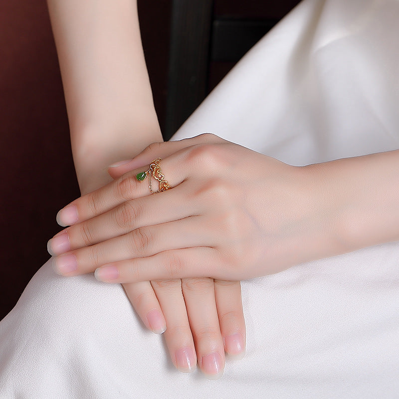 Close-up of a woman's hand wearing the Heaven's Favor Hetian Jade Cloud Ring, featuring a delicate gold band with cloud-like filigree and a dangling green jade teardrop.