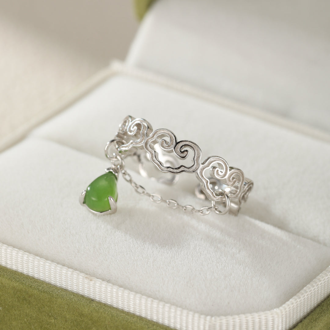 Heaven's Favor Hetian Jade Cloud Ring with a teardrop-shaped green jade charm suspended from a delicate silver chain, set against a soft, textured background within a jewelry box.