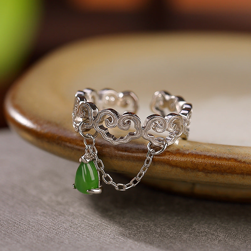 A silver ring with a cloud design and a dangling green jade teardrop charm.