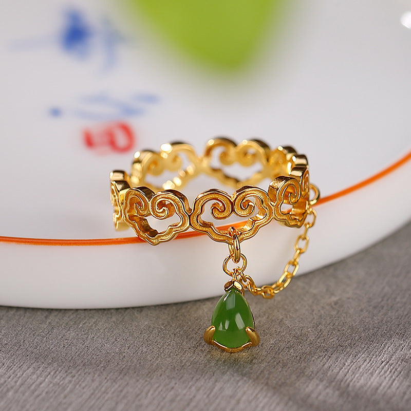 Gold ring with cloud motifs and a dangling green jade teardrop charm on a delicate chain.