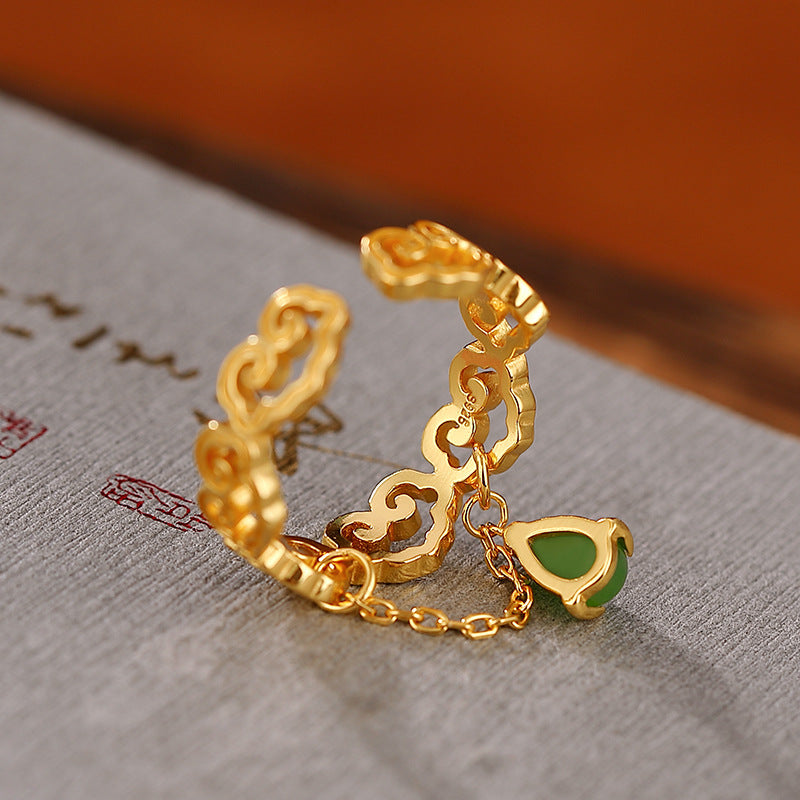 Close-up of a gold ring with cloud motifs and a dangling green jade teardrop charm.