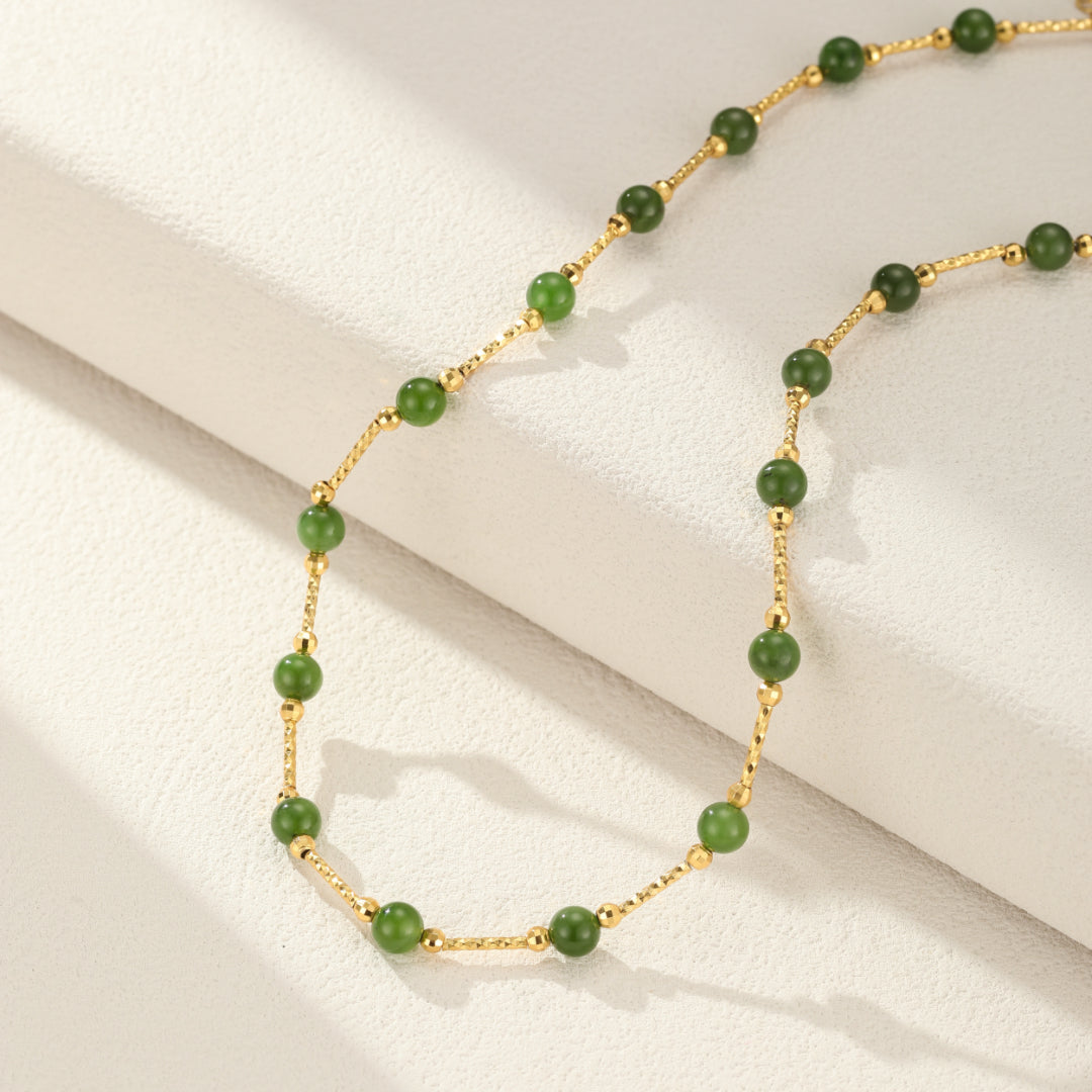 A delicate gold chain necklace featuring evenly spaced green jade beads and small gold accents.