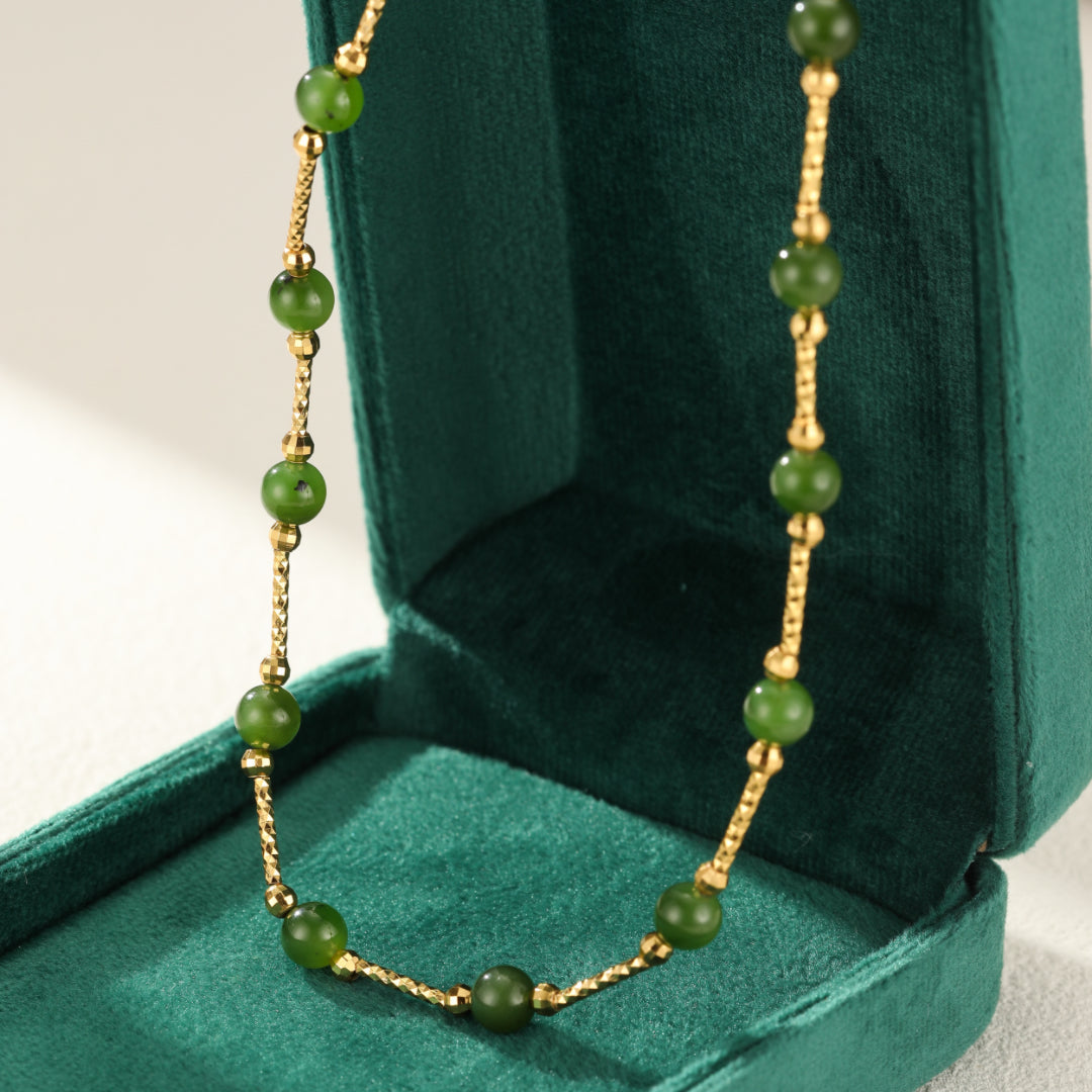 Close-up of a gold chain necklace with green jade beads, presented in a green velvet jewelry box.