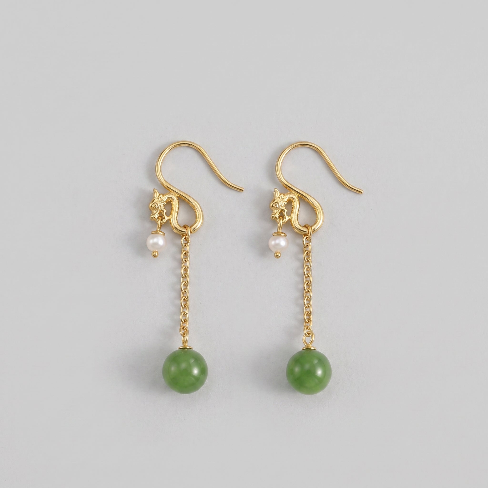 A pair of gold dragon drop earrings with green jade beads and small pearls dangling from delicate chains.